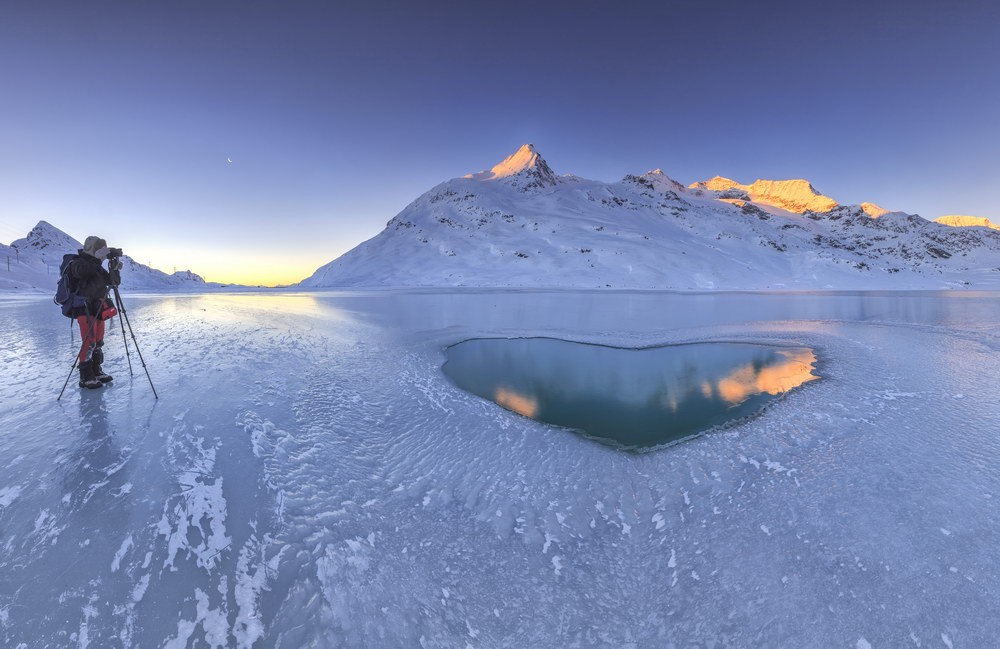 Il fotografo cattura i primi raggi del sole sulle cime innevate e un cuore d'acqua nel mezzo del Lago Bianco ghiacciato.
