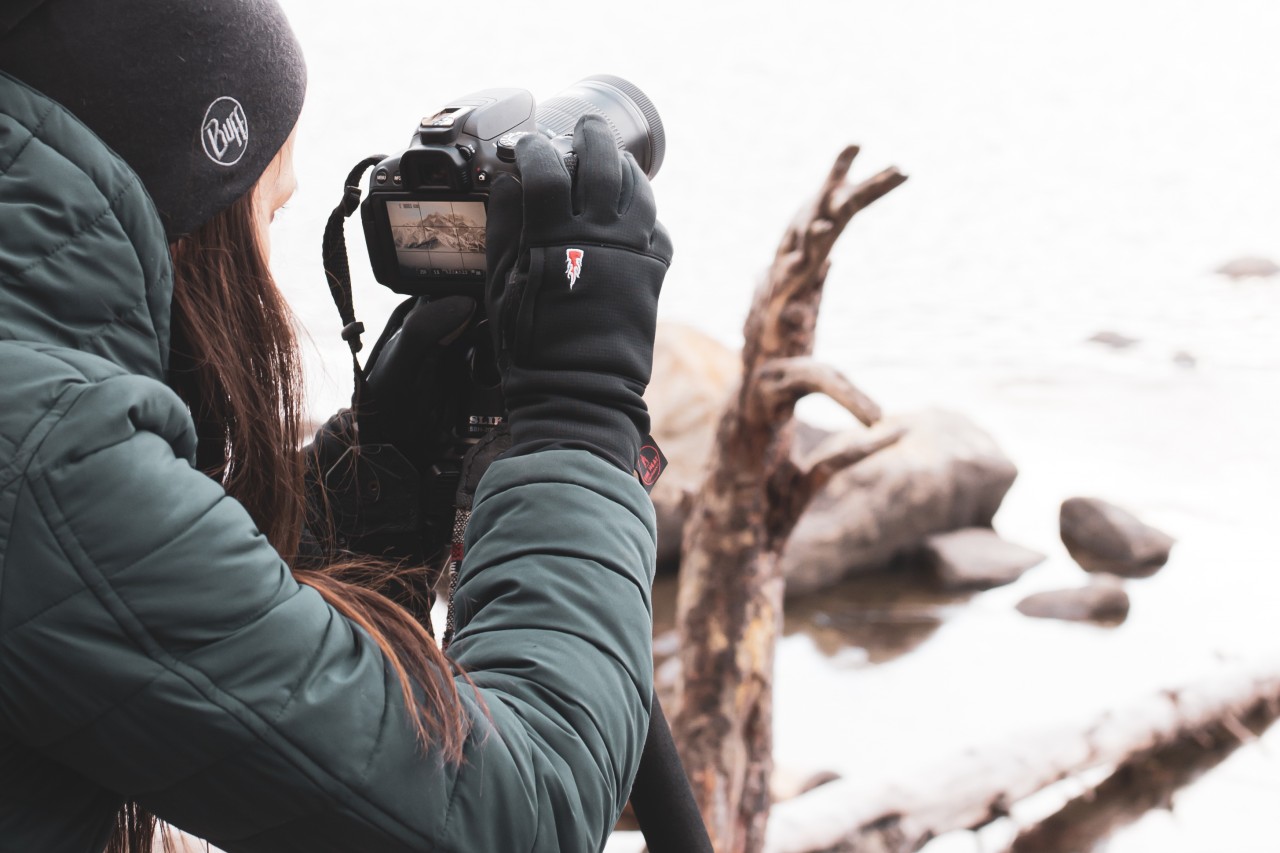 Fotografa con guanti, giacca e berretto per fotografare lo sfondo di una montagna